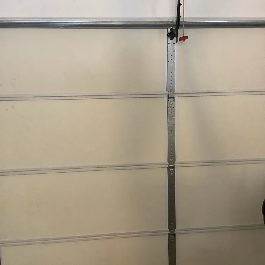 The inside of a closed sand-coloured garage door with a full-height steel reinforcement strut down the centre, the opener arm and red release handle at the top.