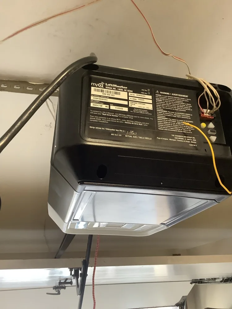 The underside of a LiftMaster myQ opener with its serial plate and warning label facing down, low-voltage wires running to the terminals on the end panel.