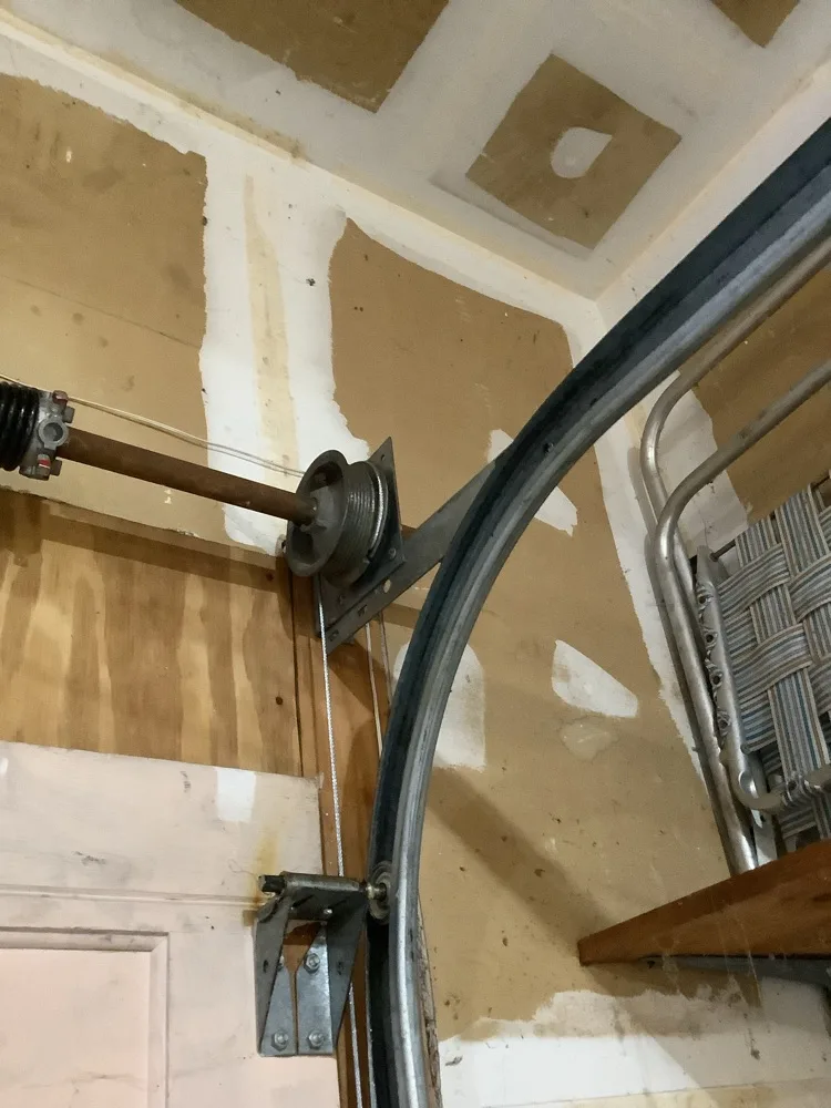 A grooved cable drum seated on the end of a torsion shaft with the lift cable wound into it and running down the inside of the curved track to the bottom bracket.